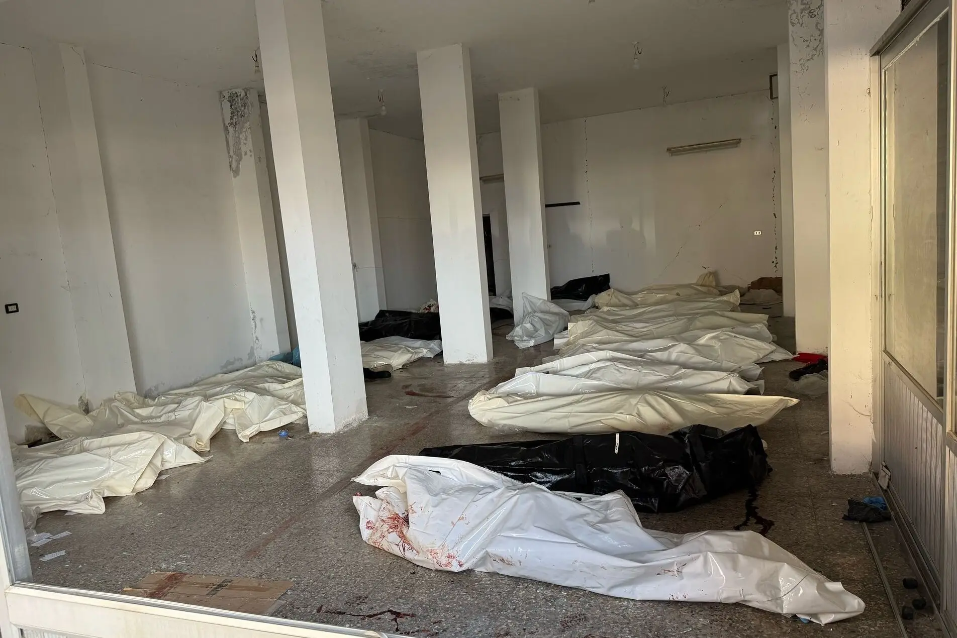 У центрі Баніяса, Сирія, на початку березня працівники служби надзвичайних ситуацій перетворили пограбований меблевий магазин на імпровізований морг, наповнений мертвими в мішках для трупів.